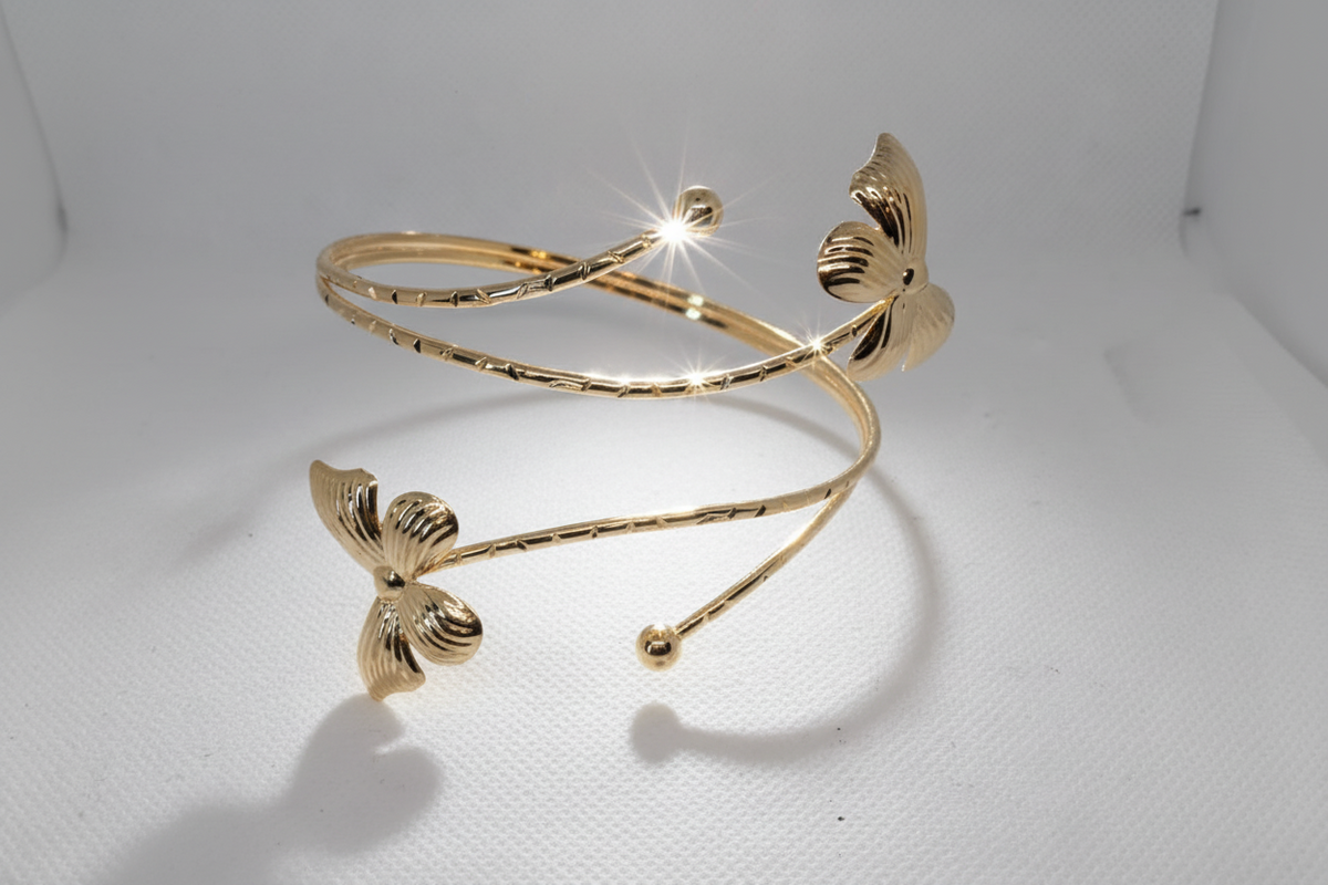 A gold-colored open cuff bangle bracelet with textured leaf-like details on both ends and small bead accents, displayed on a light gray background.